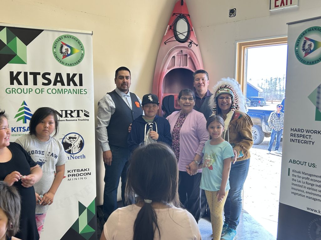 Chief Tammy Searson Cook stands proudly at a Kitsaki booth alongside the beaming winners of the Kayak giveaway, all holding their colorful new kayaks and ready for their next water adventure.